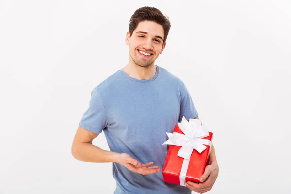 Smilende mand i t-shirt præsenterer gave og ser på kameraet - Stock-foto