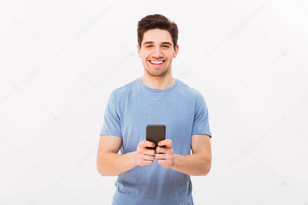 Happy man 30s in casual t-shirt typing sms or browsing internet 