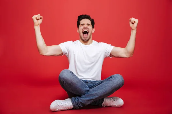 Portrét radostné mladého muže v bílé tričko sezení — Stock fotografie