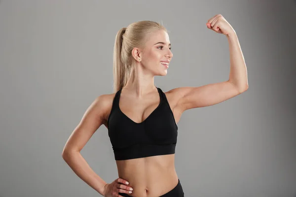 Cheerful young blonde sports lady showing biceps. — Stock Photo, Image