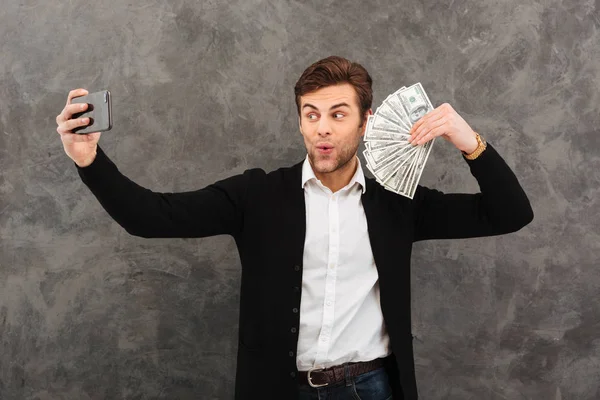 Joven empresario sorprendido sosteniendo dinero hacer selfie por teléfono móvil . — Foto de Stock