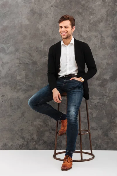 Jovem empresário alegre sentado sobre a parede cinzenta — Fotografia de Stock