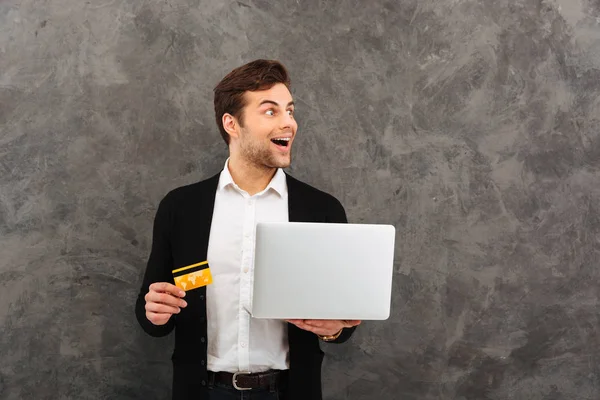 Empresário animado usando laptop computador segurando cartão de crédito . — Fotografia de Stock