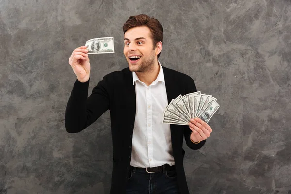 Animado jovem empresário feliz segurando dinheiro olhando para o lado . — Fotografia de Stock