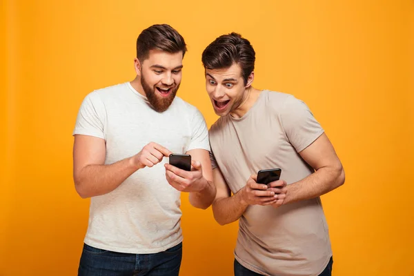 Dos hombres alegres en conversaciones informales y mirando los teléfonos móviles en — Foto de Stock