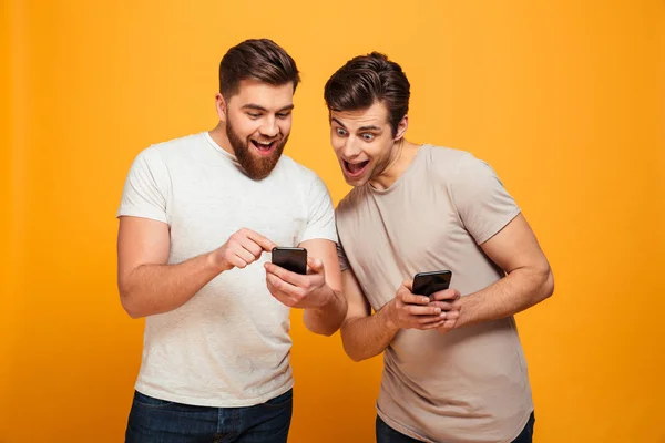 Två glada män i casual prata och titta på mobiltelefoner i — Stockfoto
