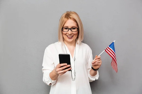 Smiling middle-aged woman in shirt and eyeglasses holding USA flag — Stock Photo, Image