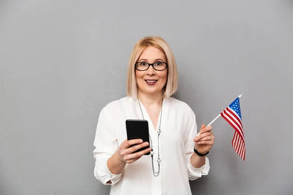 Happy middle-aged woman in shirt and eyeglasses holding USA flag — Stock Photo, Image