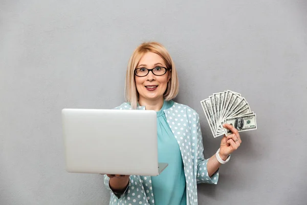 Sonriente mujer rubia de mediana edad en blusa y gafas con dinero —  Fotos de Stock