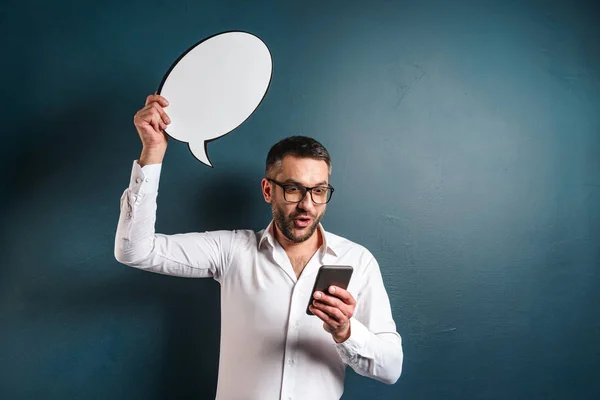 Positive man wearing glasses holding speech bubble chatting by phone.