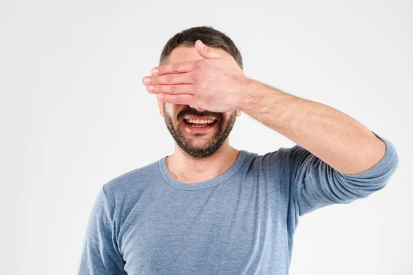 Fröhlicher junger Mann steht isoliert und bedeckt die Augen mit der Hand. — Stockfoto