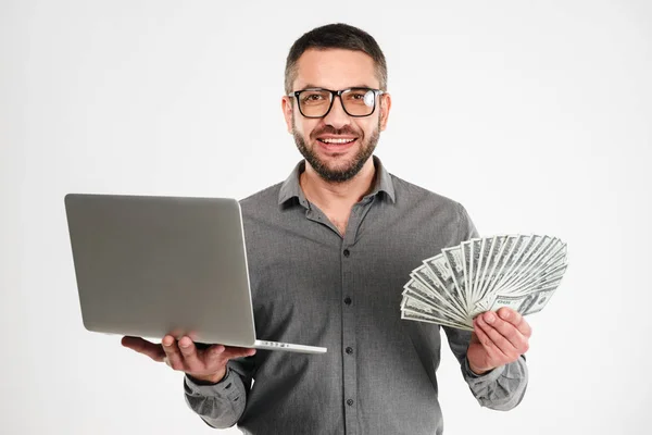 Szczęśliwy biznesmen przy użyciu komputera przenośnego, trzymając pieniądze. — Zdjęcie stockowe