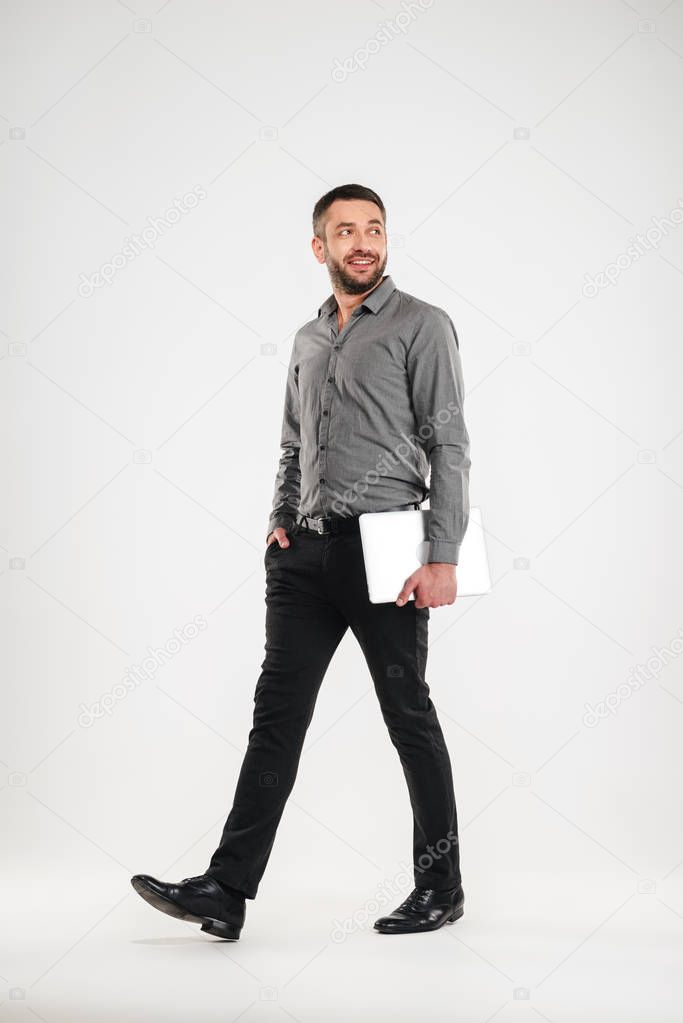 Cheerful man walking isolated holding laptop computer.
