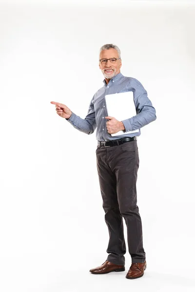 Mature grey-haired man pointing at copy space and holding laptop computer — Stock Photo, Image