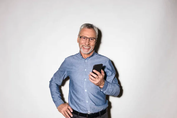 Веселый зрелый мужчина улыбаясь и держа смартфон изолирован — стоковое фото