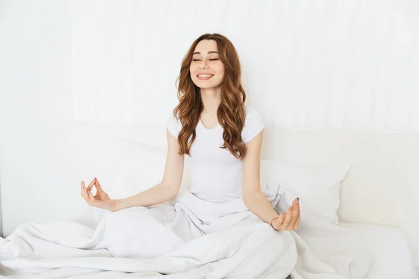 Porträt einer glücklichen jungen Frau, die im Bett meditiert — Stockfoto