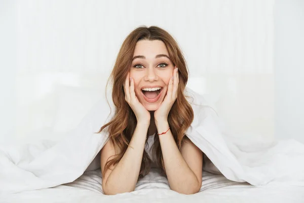 Portræt af en glad ung kvinde liggende i sengen - Stock-foto