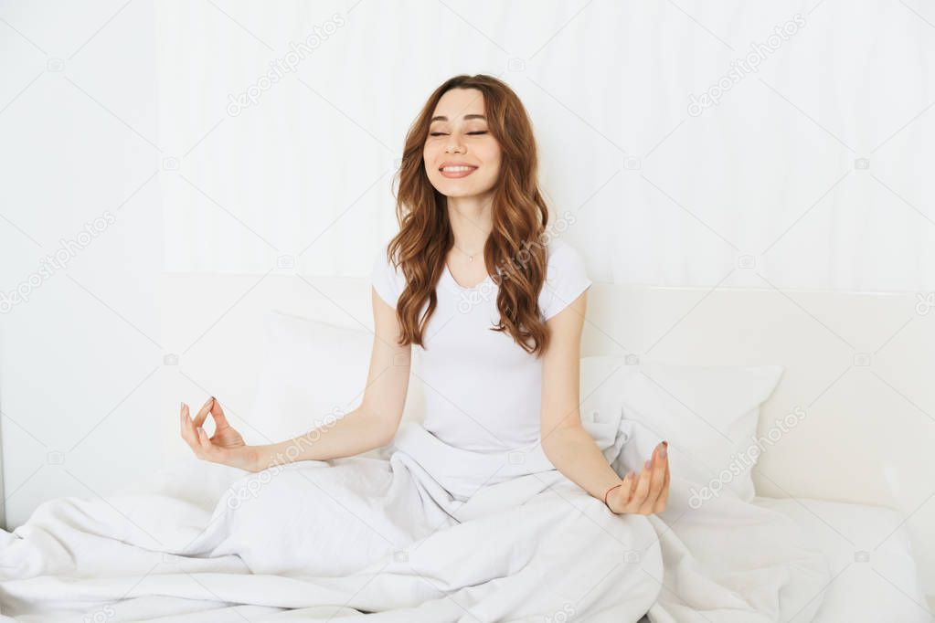 Portrait of a happy young woman meditating on bed