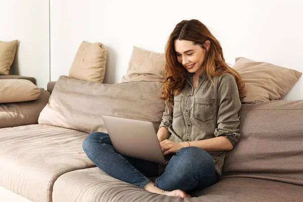 Bild einer modernen Frau mit braunen Haaren, die auf dem Sofa im Wohnzimmer sitzt — Stockfoto