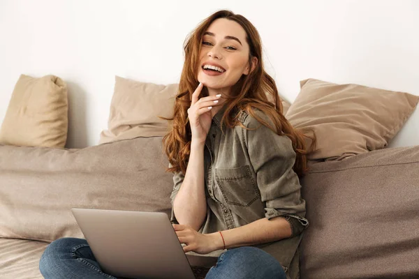 Bild einer fröhlichen Frau in den 20er Jahren mit braunen Haaren, die auf einem Sofa im Wohnzimmer sitzt — Stockfoto