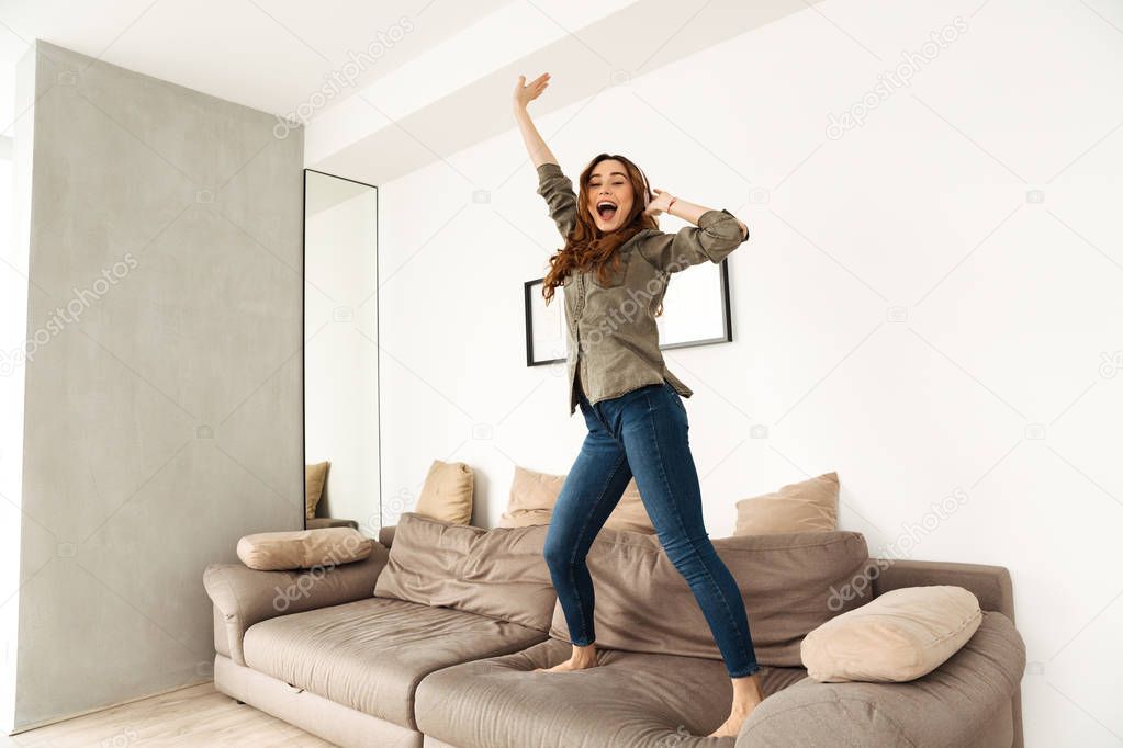Image of cheerful woman 20s in casual clothing dancing on couch 
