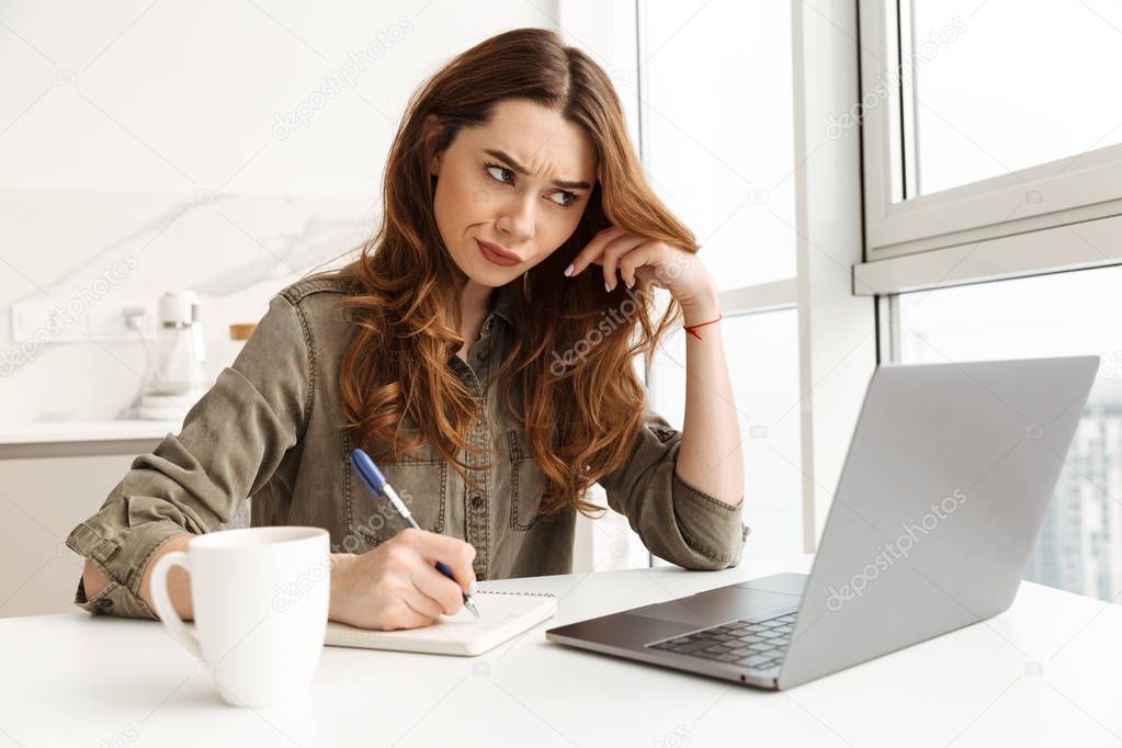 Concentrated woman 20s working in kitchen at home, and writing d