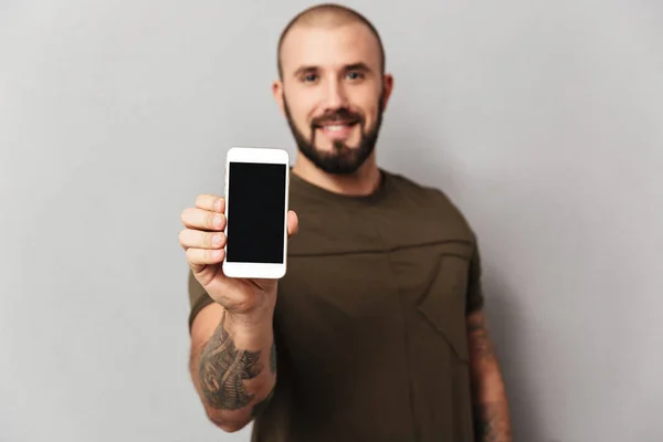 Retrato de sorrir homem musculoso 30 anos com barba mostrando smartpho — Fotografia de Stock