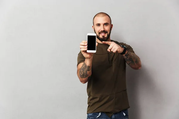 Well-built happy man 30s holding mobile phone and pointing finge