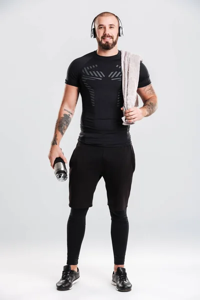Foto de un hombre sano con auriculares sosteniendo la toalla y la botella — Foto de Stock