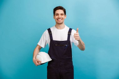 Koruyucu kask tutarak ve başparmak gösterilmesini gülümseyen erkek Oluşturucu