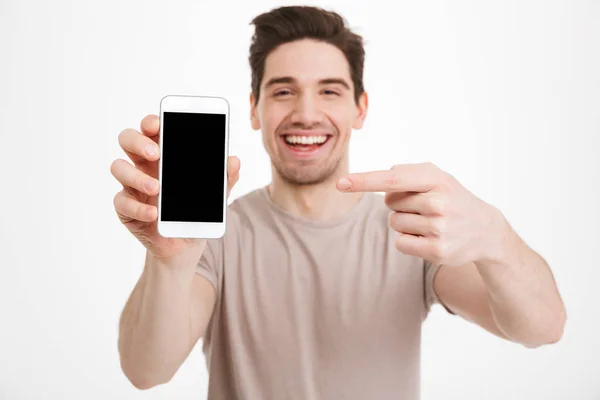 Hombre joven en camiseta casual demostrando teléfono móvil y punto — Foto de Stock