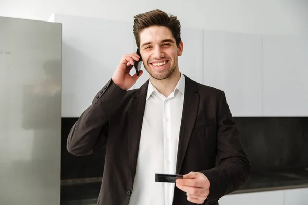 Heureux jeune homme d'affaires parlant par téléphone portable tenant carte de crédit . — Photo