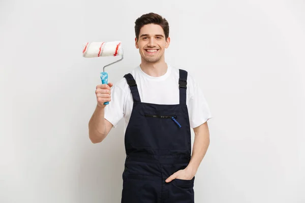 Constructor masculino sonriente con brazo en bolsillo sosteniendo rollo de pintura — Foto de Stock