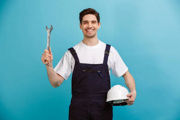 Pleased male builder holding protective helmet and wrench — Stock Photo, Image