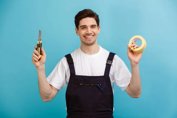 Constructor masculino sonriente que sostiene el cortador y la cinta adhesiva — Foto de Stock