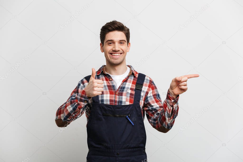Smiling male builder pointing away and showing thumb up