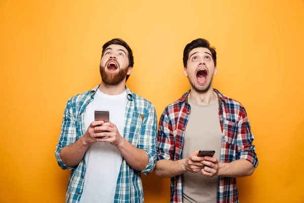 Porträtt av två glada unga män håller mobiltelefoner — Stockfoto