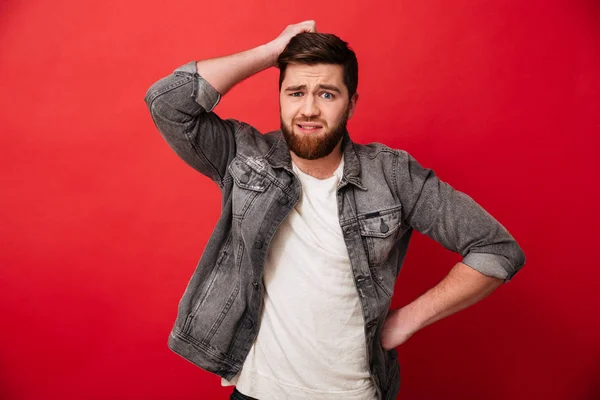 Upset man 30s in jeans jacket looking on camera and scratching h — Stock Photo, Image