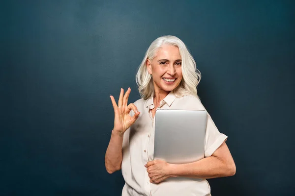 Зріла весела стара жінка, що показує добре жест тримає ноутбук комп'ютера . — стокове фото