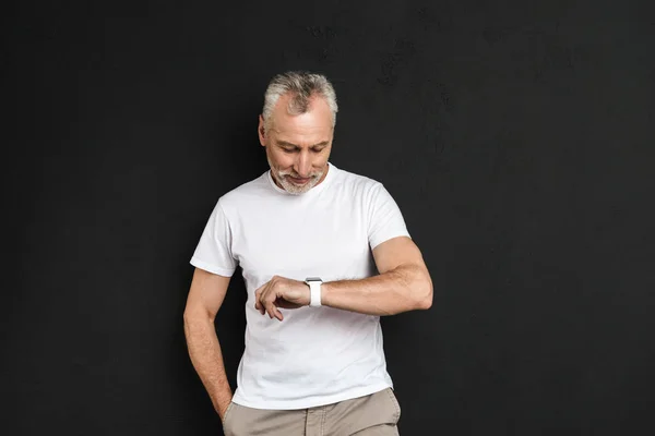 Cheerful mature old man standing isolated looking at his watch. — Stock Photo, Image
