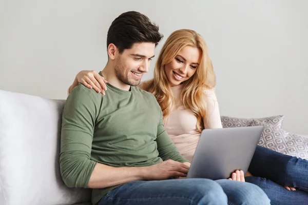 Linda pareja amorosa joven sentado en el sofá utilizando el ordenador portátil . —  Fotos de Stock