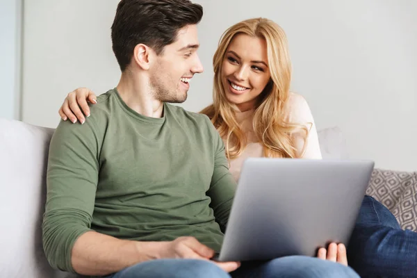 Nettes junges Liebespaar sitzt auf Sofa mit Laptop-Computer. — Stockfoto