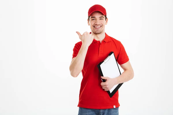 빨간 유니폼 웃 고 가리키고 있는 젊은 택배 남자 손가락 asi — 스톡 사진