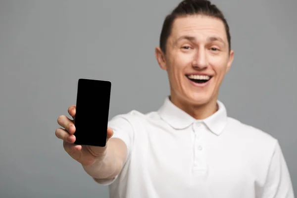 Joven alegre parado aislado mostrando la pantalla del teléfono móvil . — Foto de Stock