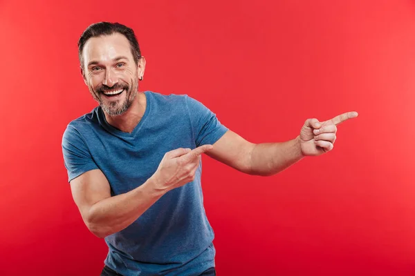 Happy unshaved man 30s in casual blue t-shirt pointing fingers a — Stock Photo, Image