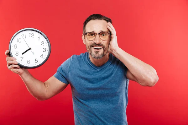 Verwarde man in kleurrijke zonnebril holding klok. — Stockfoto