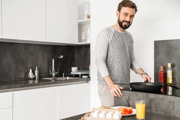 Single happy man wearing casual clothing cooking dinner on fryin