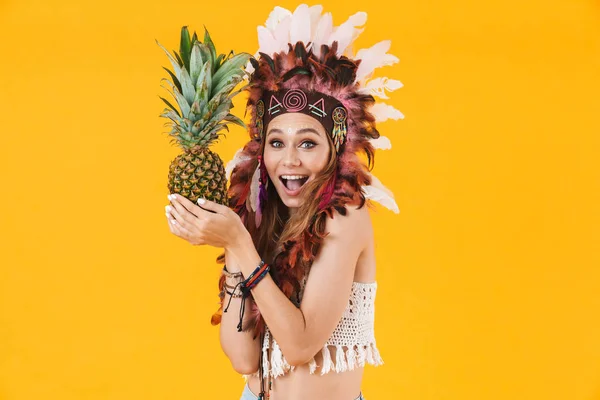 Porträt einer entzückten süßen Frau mit Federkopfschmuck, die Ananas hält und lächelt — Stockfoto
