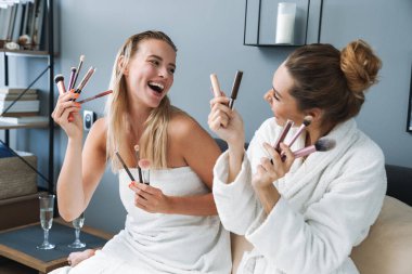 Women friends sisters after spa procedure holding makeup brushes. clipart