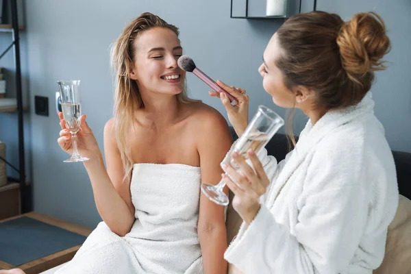 Vänner systrar inomhus gör makeup med makeup borste dricka champagne. — Stockfoto